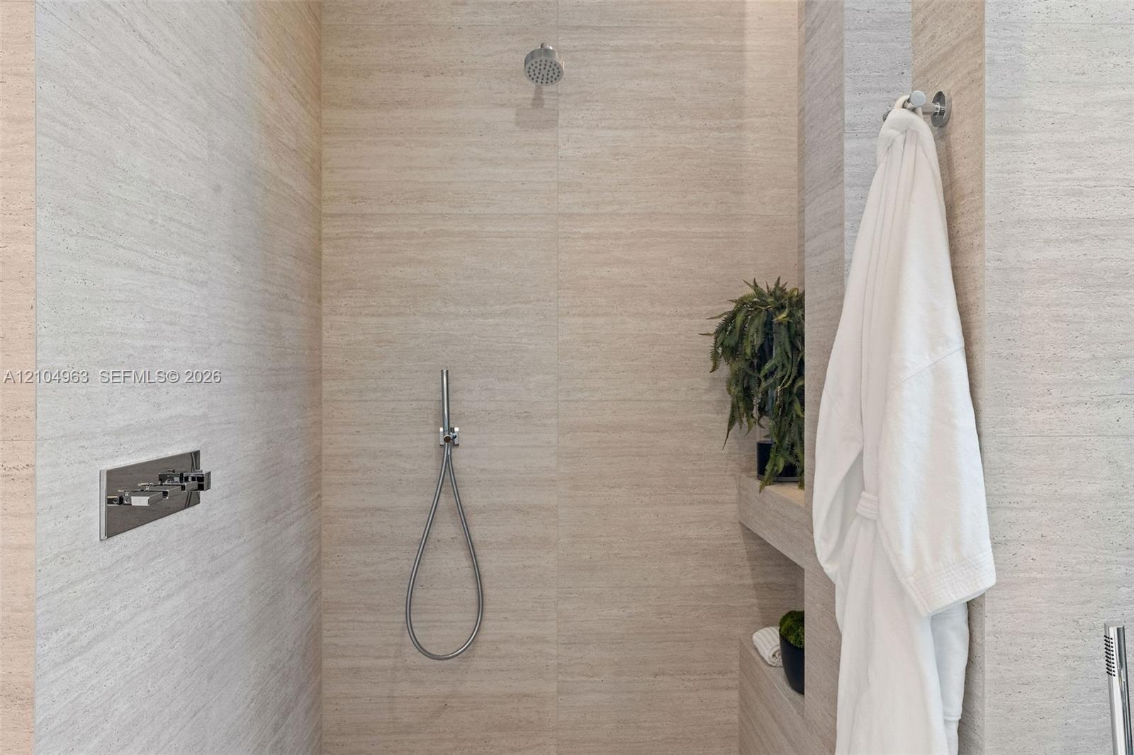 Walk-in shower featuring large-format textured stone wall tile, built-in shelving, a rainfall showerhead, and a wall-mounted handheld shower fixture w