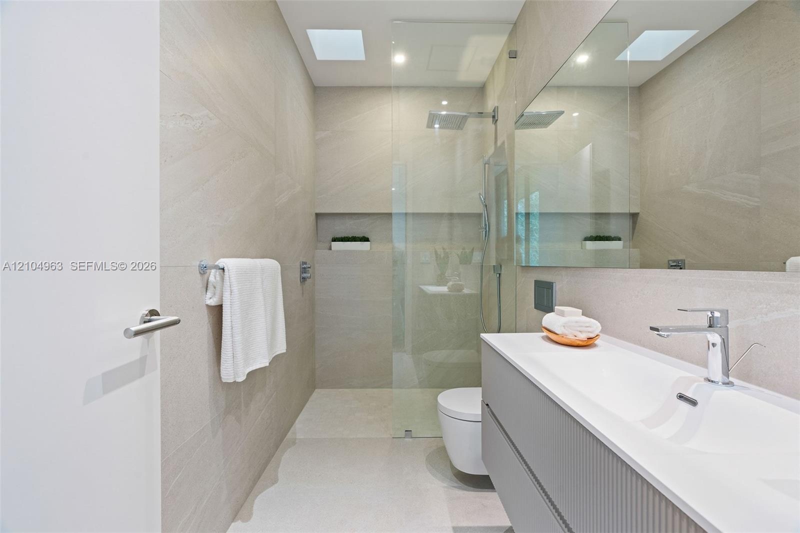 Modern bathroom featuring floor-to-ceiling textured wall tiling, a floating vanity with a seamless integrated sink, a glass-enclosed shower with a bui