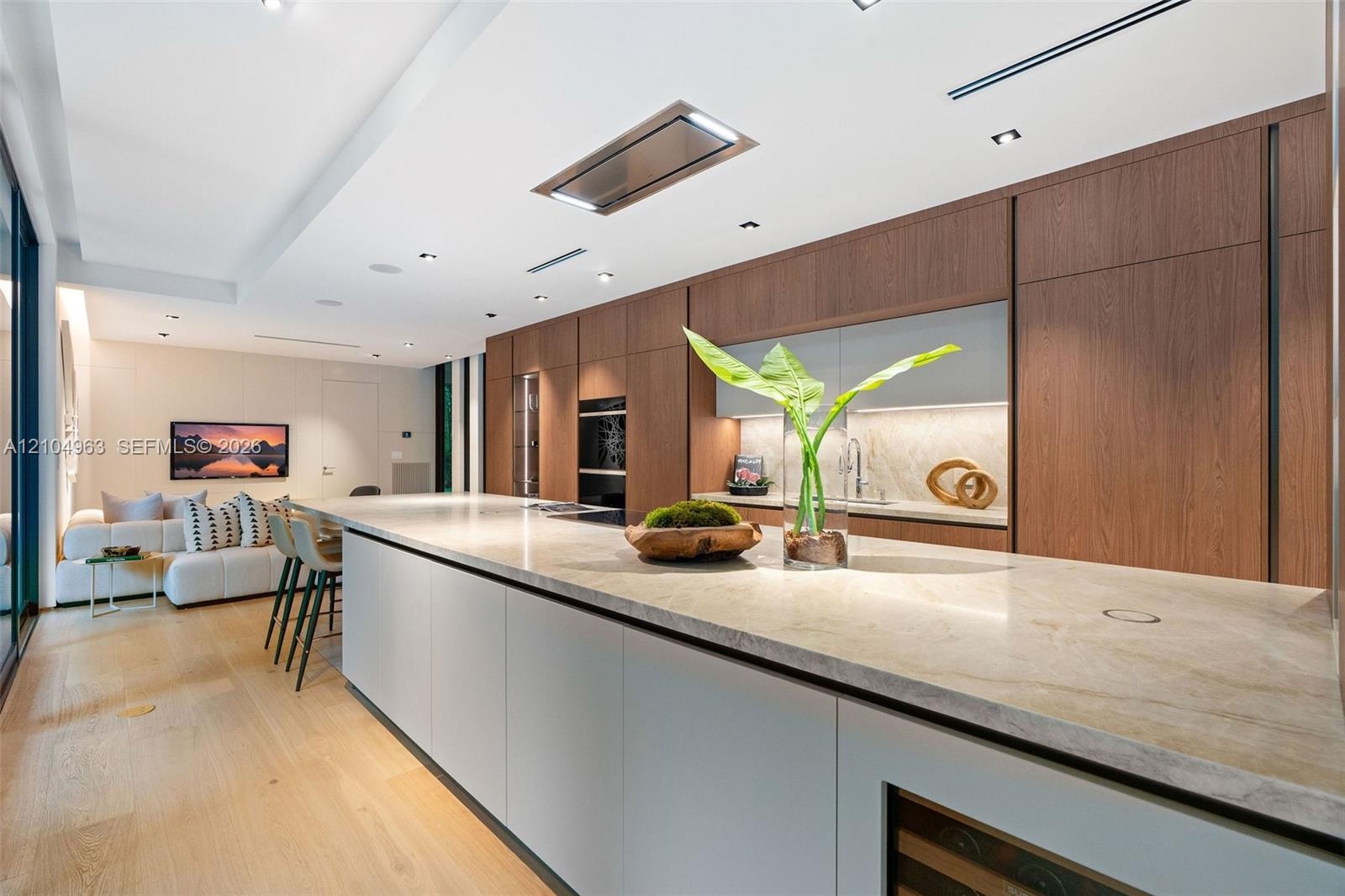 Kitchen featuring full-height wood-finish cabinetry, a lengthy stone-surfaced island, integrated double wall ovens, a built-in wine refrigerator, and 