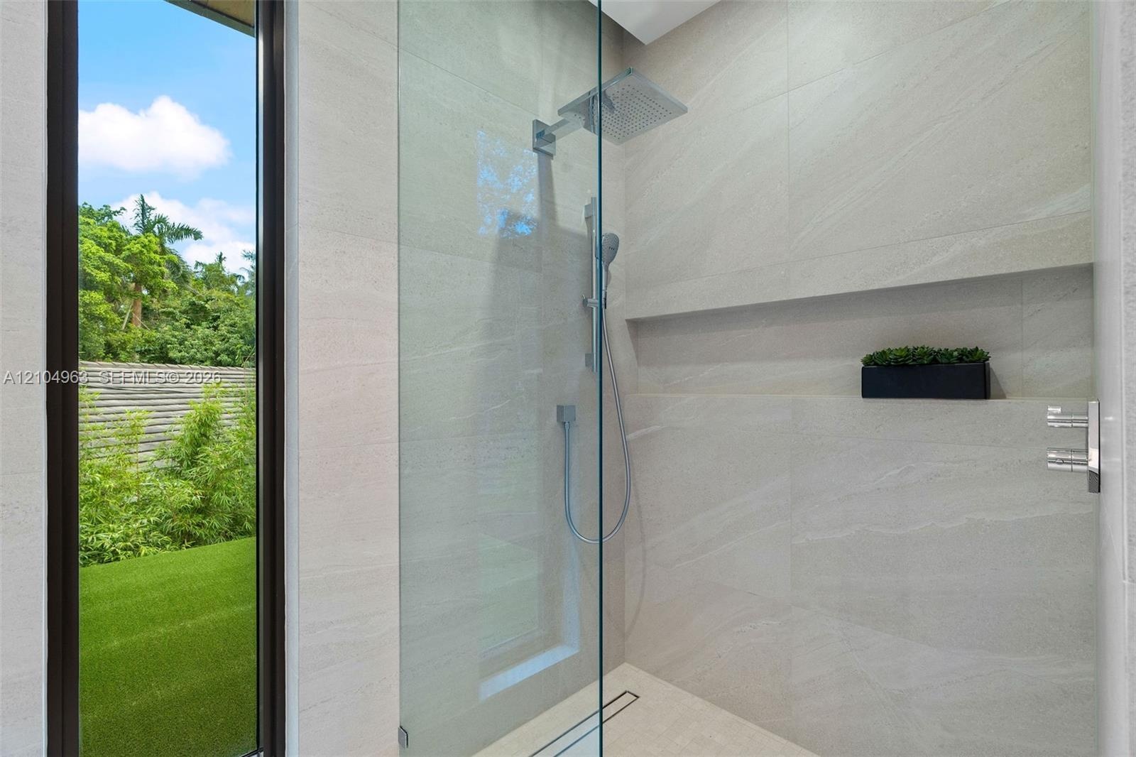 Walk-in shower featuring floor-to-ceiling stone-finish tile, frameless glass enclosure, rainfall shower head, handheld sprayer, and an integrated rece
