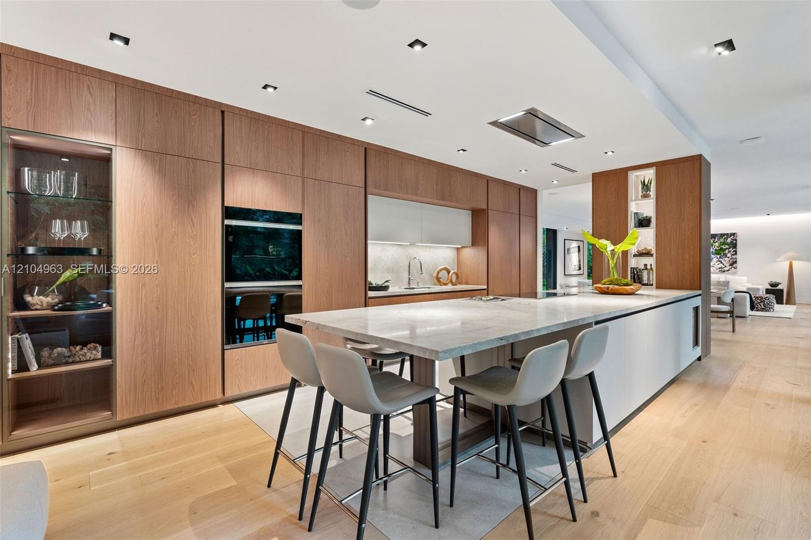 Kitchen featuring flat-panel wood cabinetry, integrated stainless steel double wall ovens, a stone-topped island with waterfall edge, and wood-finish 