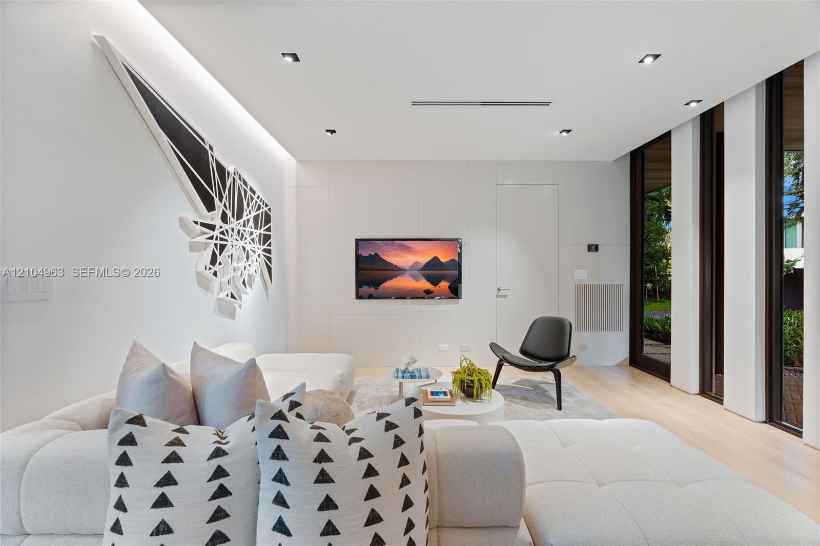 Contemporary interior featuring smooth wall panels, light-toned wood-finish flooring, recessed ceiling lighting, and floor-to-ceiling windows with dar