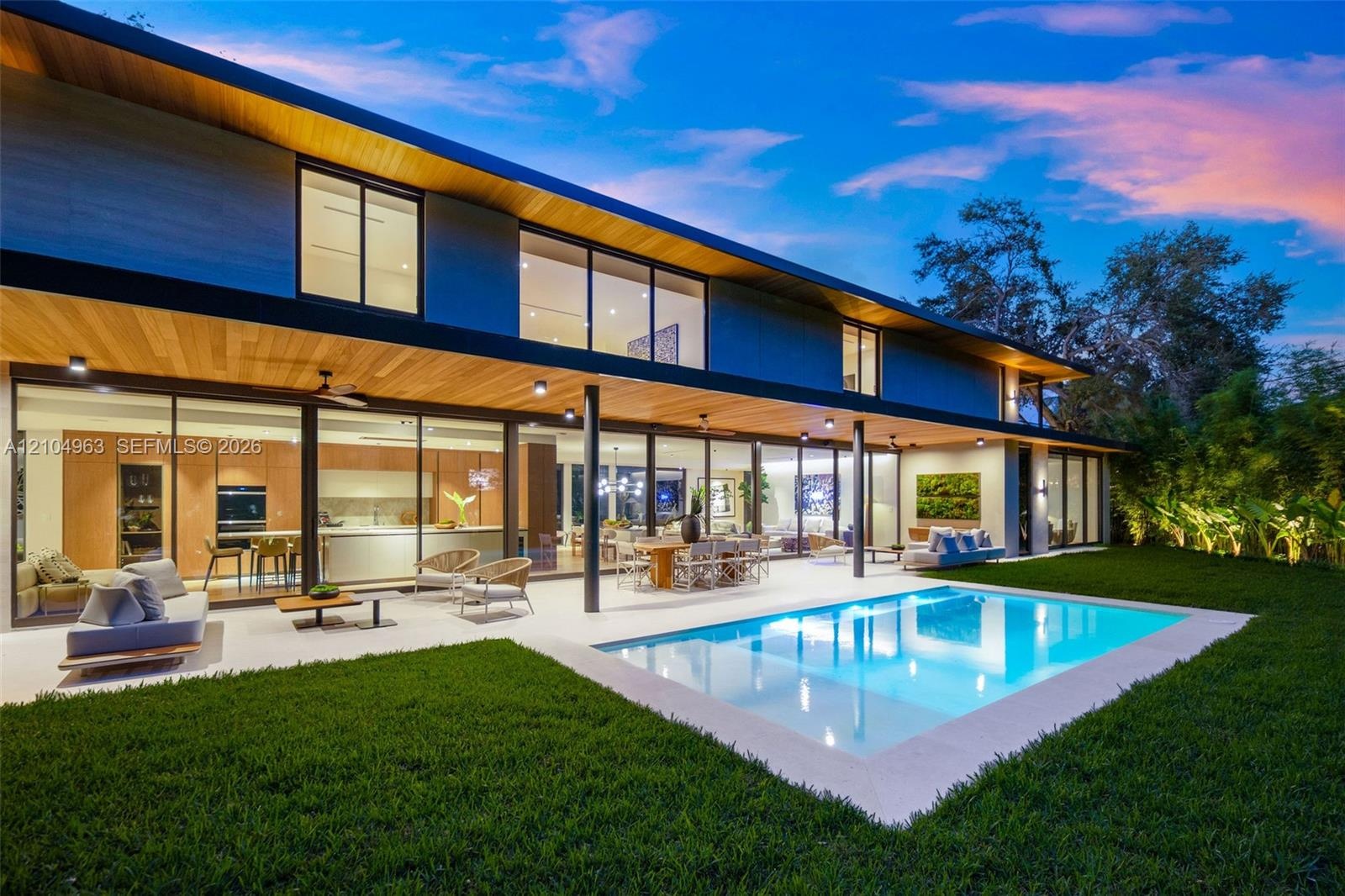 Modern two-story exterior featuring expansive floor-to-ceiling glass wall systems, a recessed wood-paneled ceiling, a rectangular in-ground swimming p