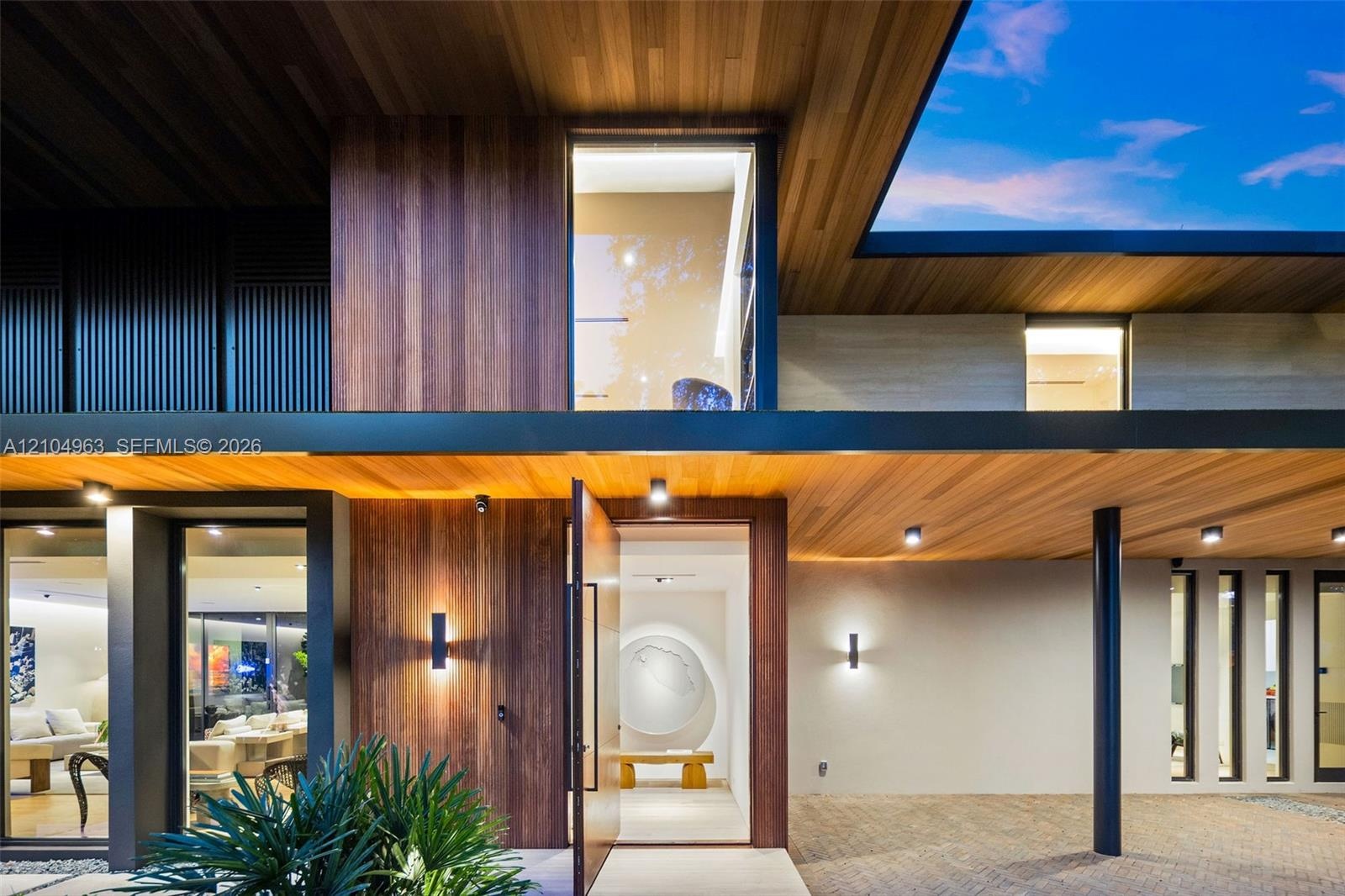 Contemporary facade featuring extensive wood-paneled cladding, floor-to-ceiling glass windows, recessed ceiling lighting, a wide pivot entry door, and