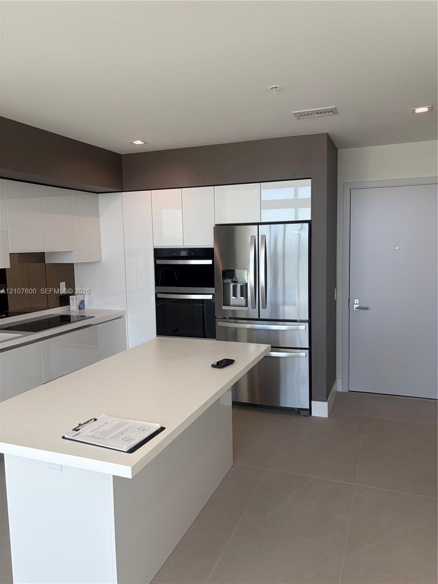 Kitchen featuring a central island with a solid surface countertop, high-gloss white cabinetry, stainless steel appliances including a built-in wall o