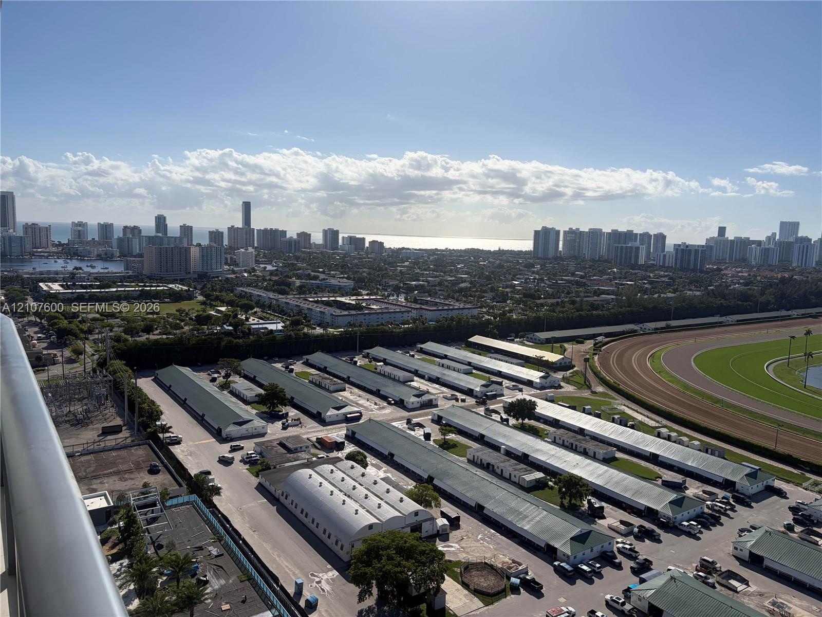 Elevated perspective featuring coastal city skyline, ocean horizon, and racetrack grounds