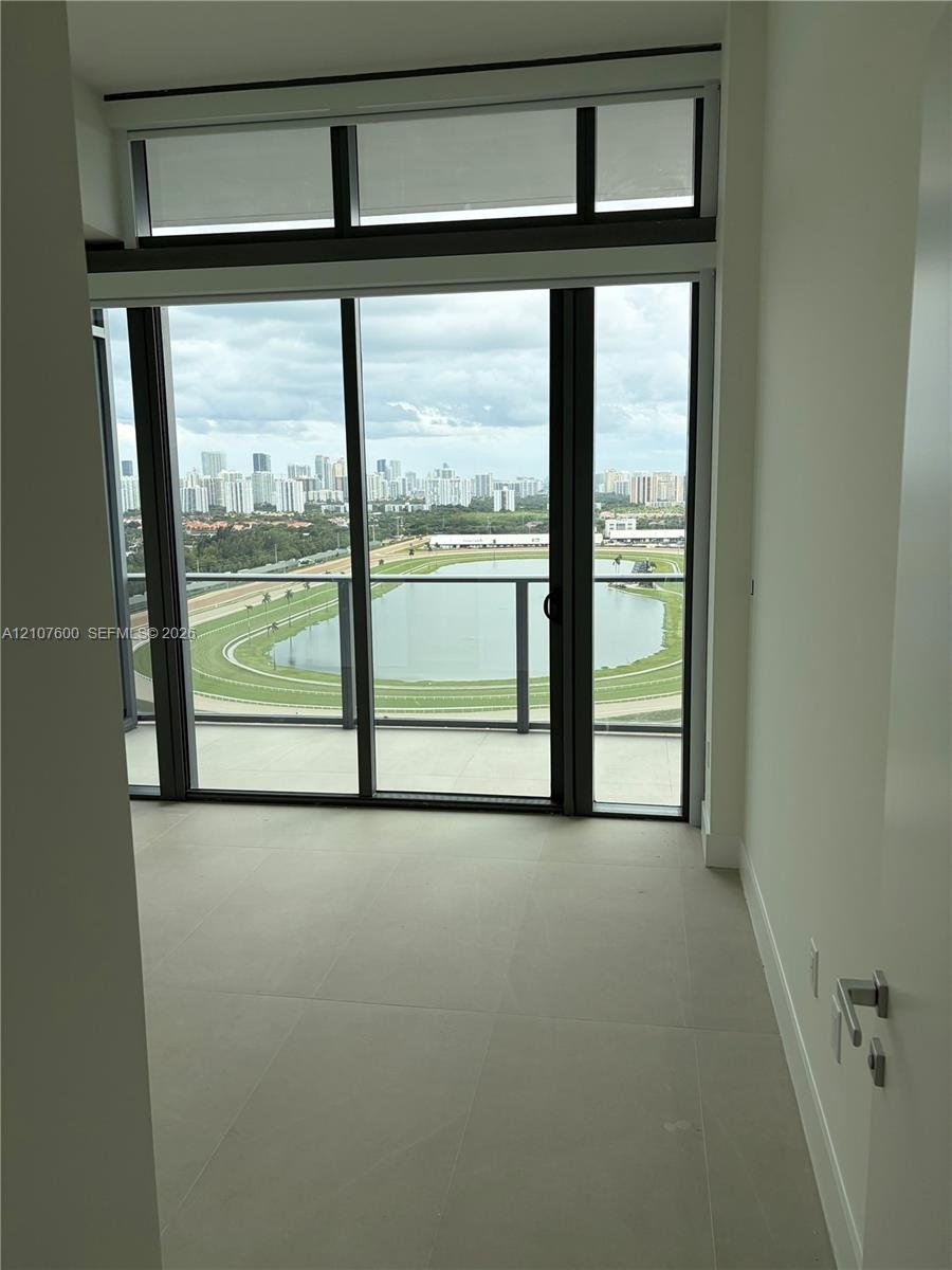 Floor-to-ceiling glass wall with sliding door access to a balcony, complemented by large-format neutral tile flooring