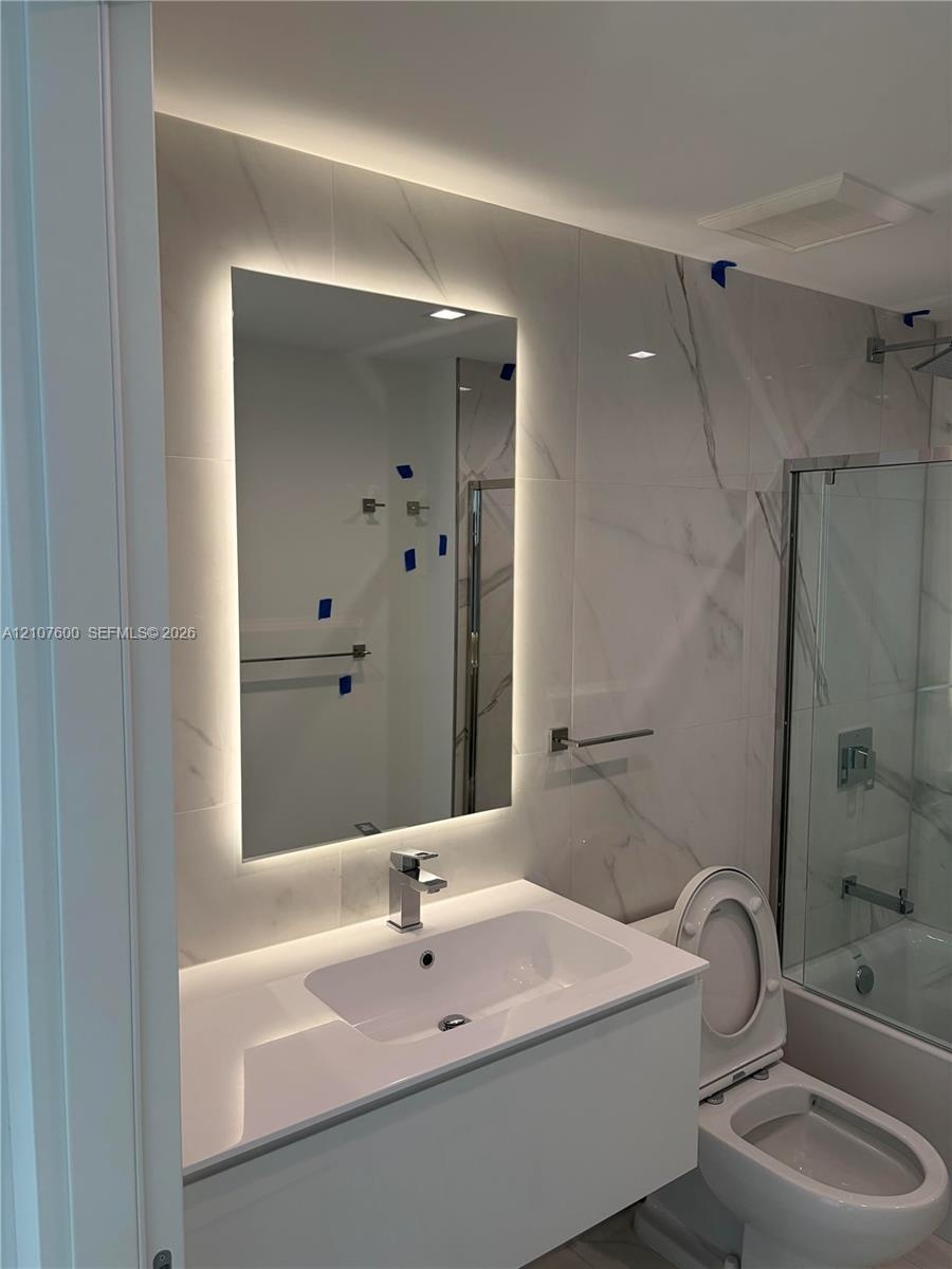 Floating vanity with a white countertop and rectangular basin, integrated backlit mirror, full-height tile wall, and glass-enclosed shower