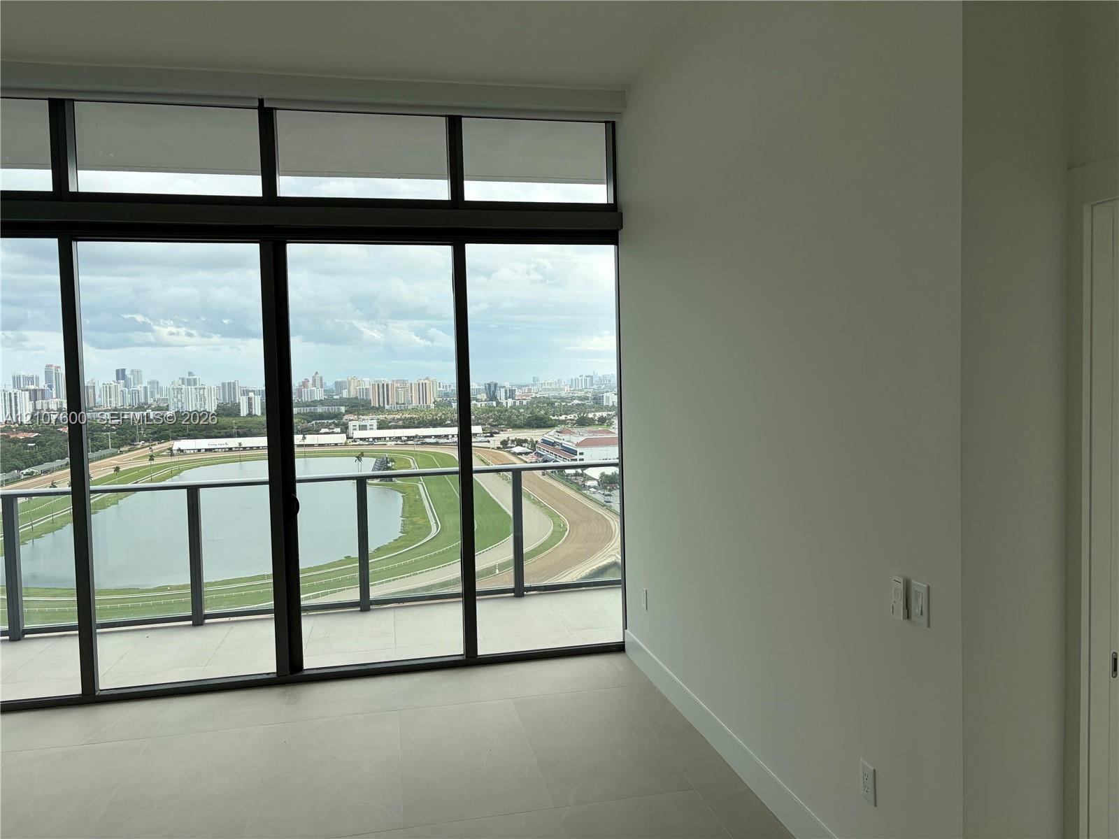 Floor-to-ceiling windows with clerestory panels, sliding glass door access to a private balcony, metal railing, and neutral large-format tile flooring