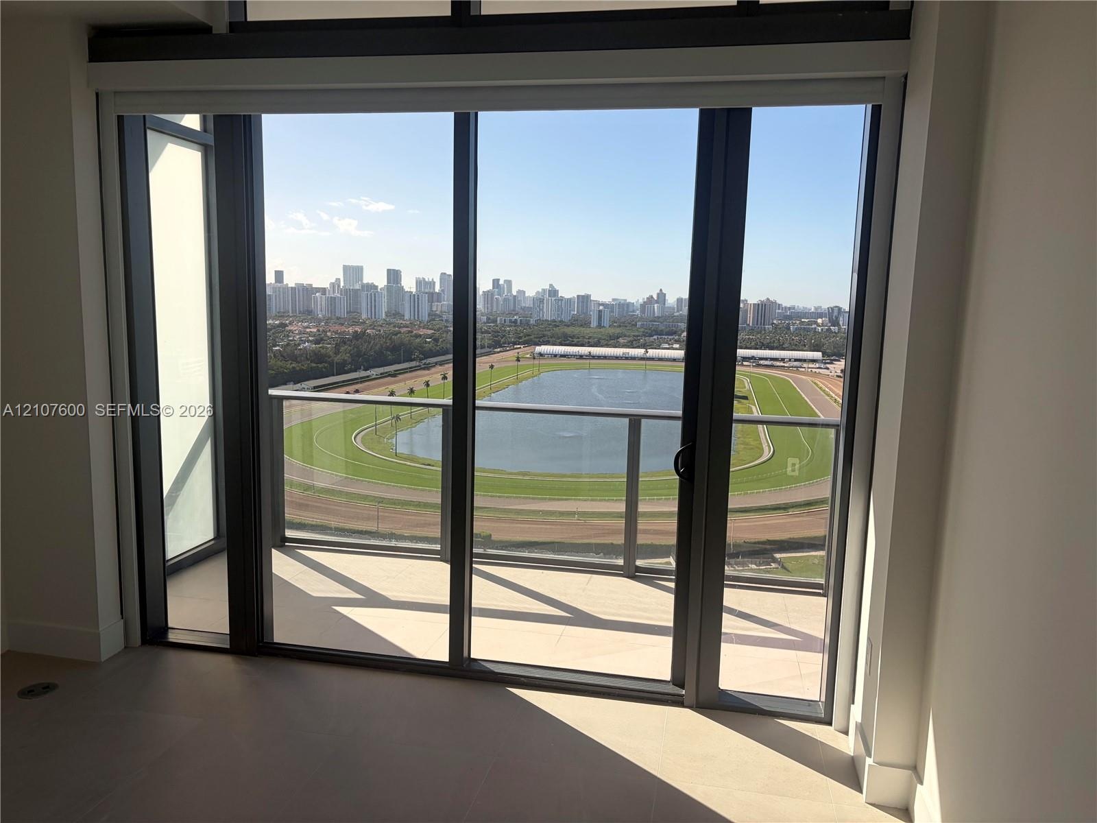 Floor-to-ceiling glass sliding doors opening to a covered balcony with a glass panel railing, tile flooring, and expansive panoramic scenery of a race