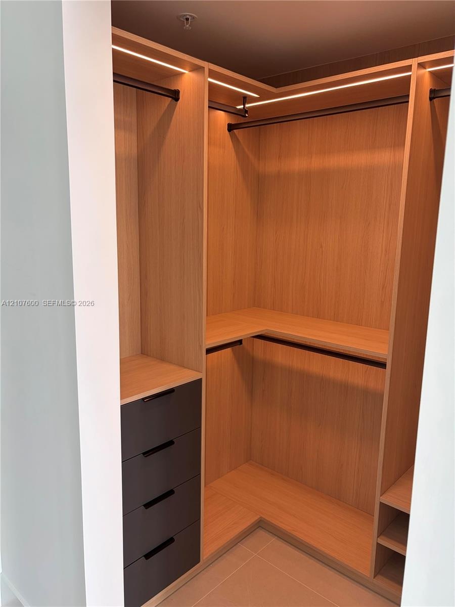 Custom walk-in closet featuring light wood-finish cabinetry, integrated linear LED lighting, dark matte drawers, and multiple hanging rods