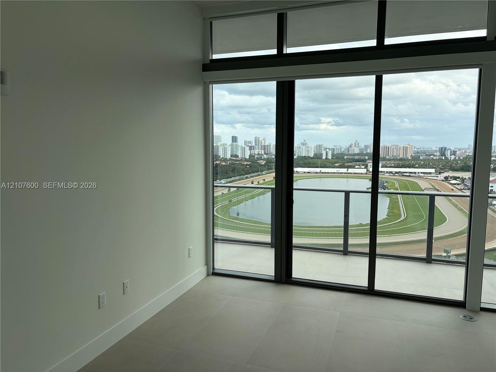 Floor-to-ceiling glass windows, ceramic tile flooring, and a glass-paneled balcony overlooking the racetrack and city skyline
