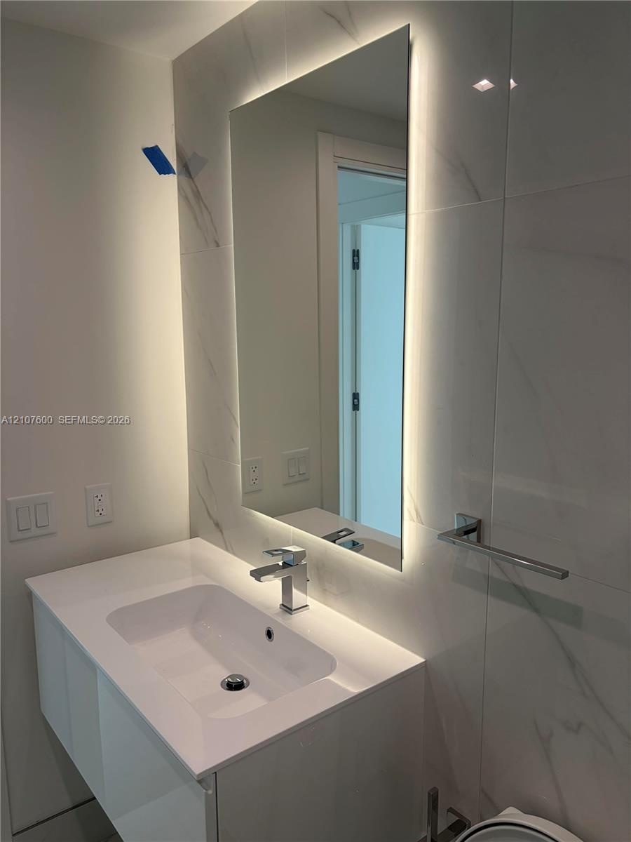 Wall-mounted vanity with integrated sink and single-handle faucet, backlit rectangular mirror, and large-format porcelain tile wall surround