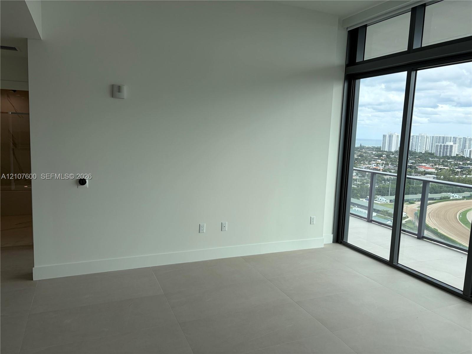 Large-format tile flooring, floor-to-ceiling glass sliding doors, and a private balcony featuring a metal railing