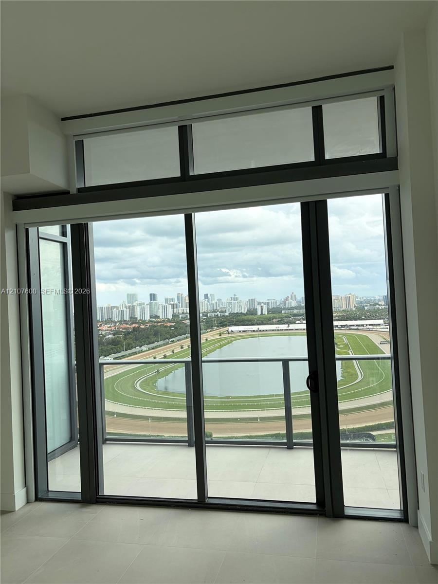 Floor-to-ceiling glass sliding doors with an upper transom window, balcony access, and railing overlooking a racetrack and cityscape