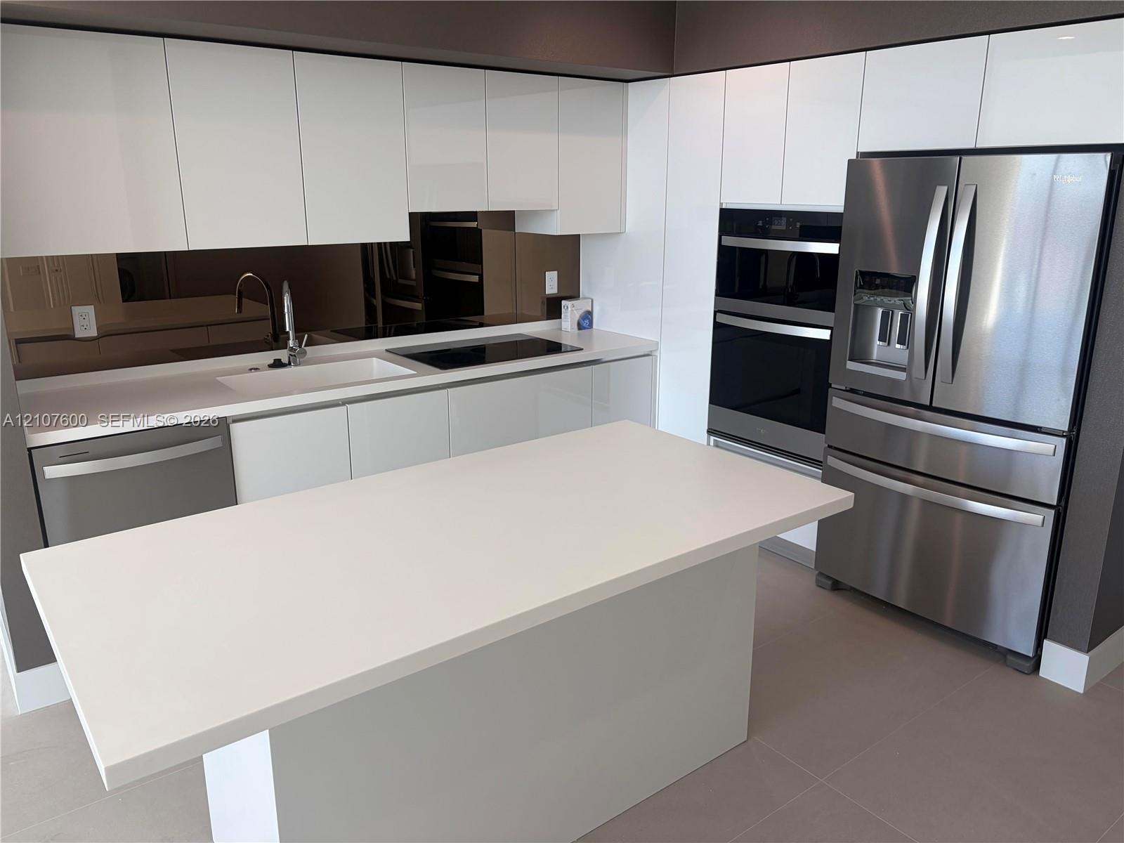 Kitchen featuring white high-gloss cabinetry, stone-surface countertops, a mirrored backsplash, stainless steel appliances, and a central island with 