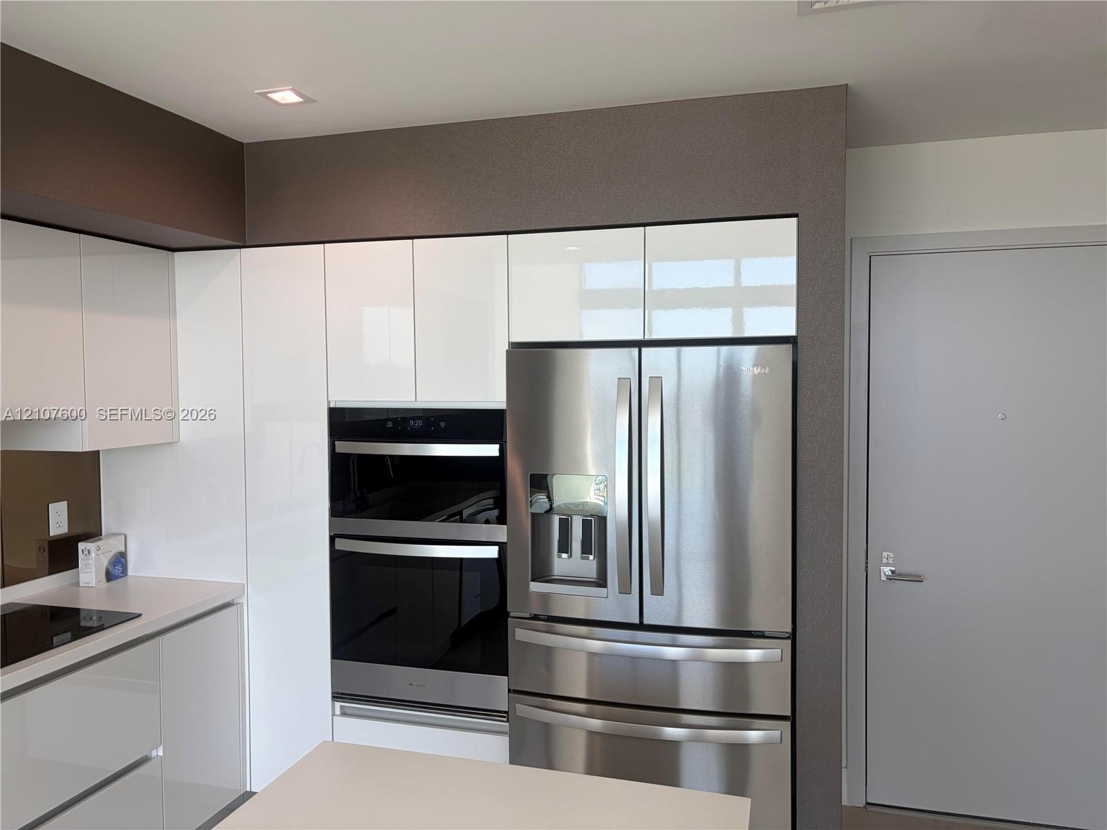 Glossy white cabinetry, built-in stainless steel double wall ovens, integrated stainless steel refrigerator, and recessed lighting