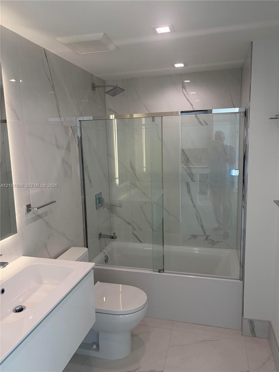 Modern bathroom featuring full-height large-format stone-patterned wall tile, a floating vanity with an integrated basin, and a glass-enclosed shower 
