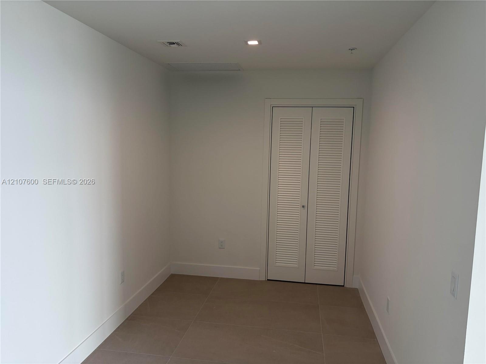 Neutral-toned oversized tile flooring and a double-door closet featuring white louvered panels and recessed lighting- Could be use as a 3rd Bed, Famil