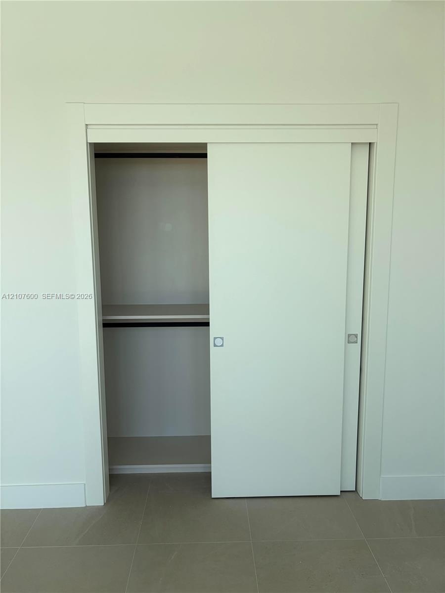 Minimalist closet featuring clean-lined sliding doors, integrated shelf, interior hanging rod, and recessed metal pulls