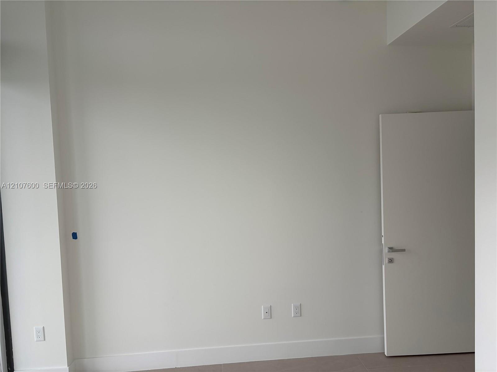 Neutral-toned interior space featuring smooth wall surfaces, a solid-core interior door, and modern lever-style door hardware