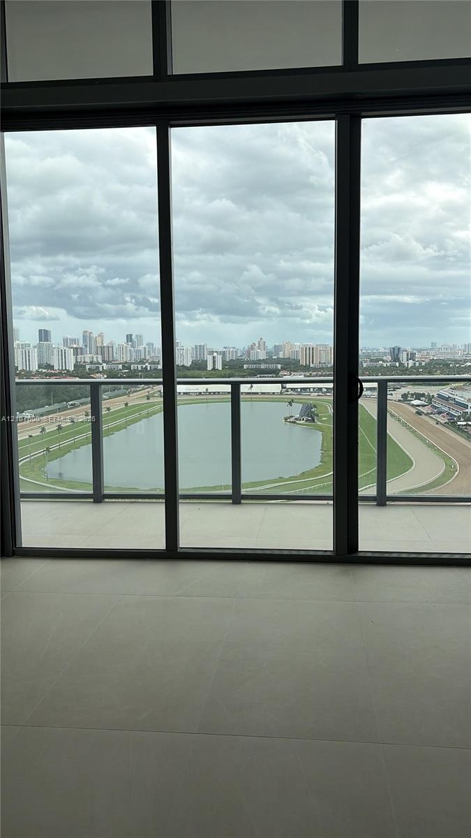 Floor-to-ceiling glass panel windows, sliding glass door, neutral large-format tile flooring, and private balcony featuring a glass railing