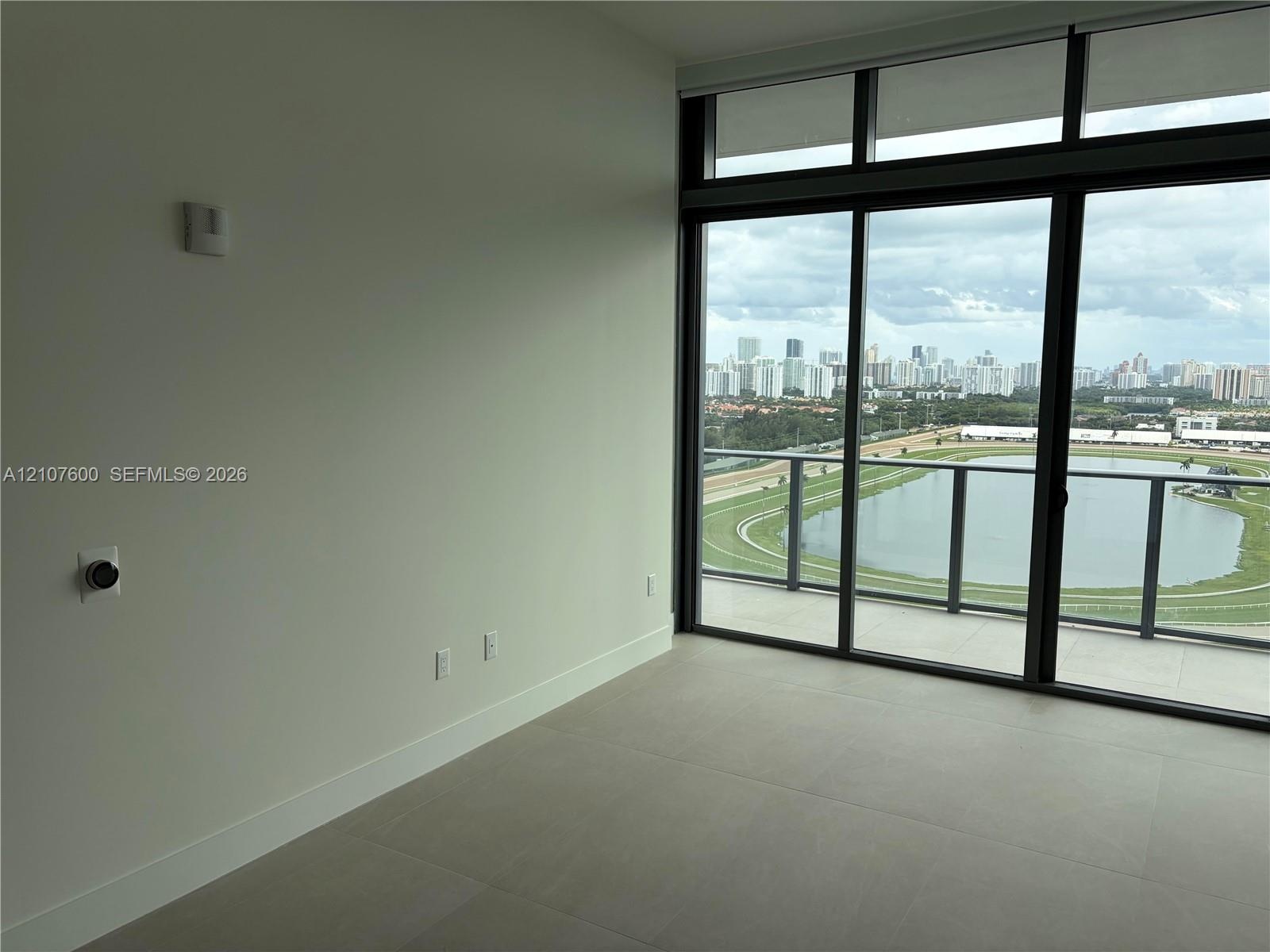 Floor-to-ceiling windows featuring panoramic city and water scenery, large-format tile flooring, and a private balcony with glass railing