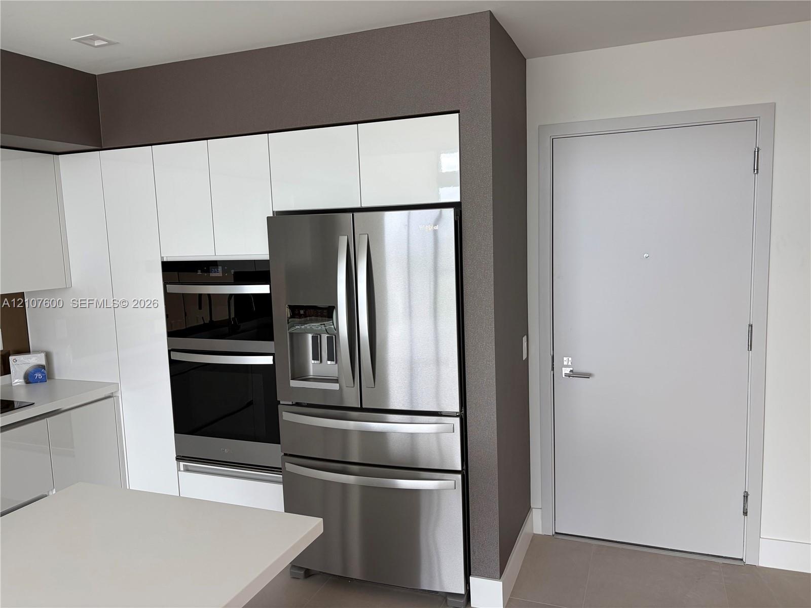 Kitchen featuring flat-panel white cabinetry, integrated stainless steel double wall ovens, a stainless steel French-door refrigerator, and solid-surf