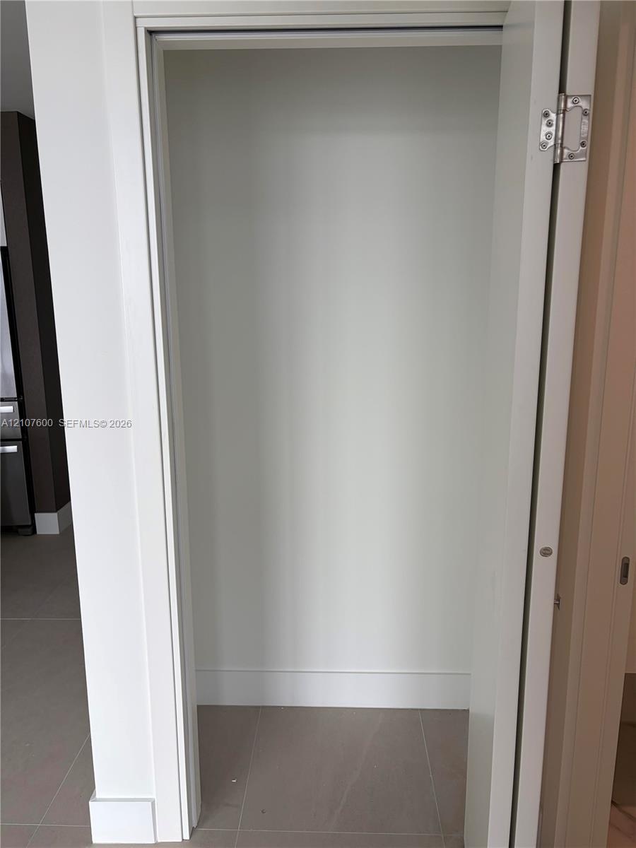 Closet featuring white painted interior, clean-lined door frame, and large-format neutral tile flooring