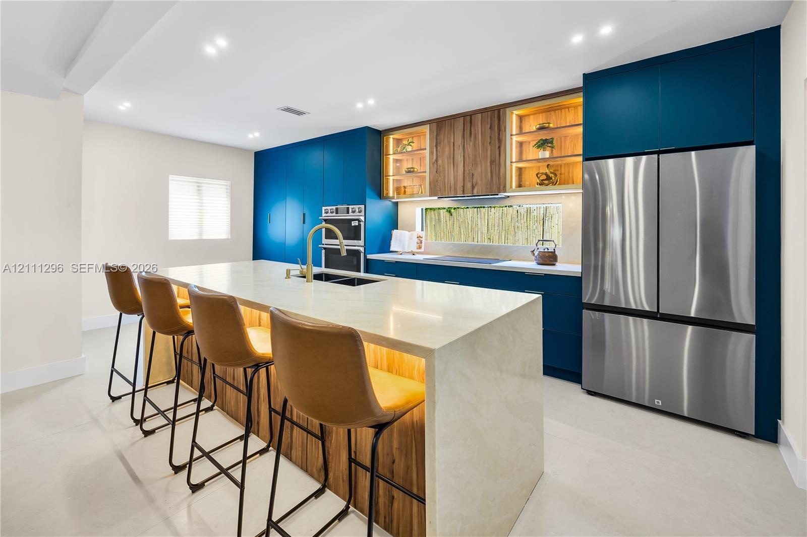 Custom kitchen featuring flat-panel blue cabinetry, expansive stone-surface island with integrated wood-finish base, stainless steel built-in double w