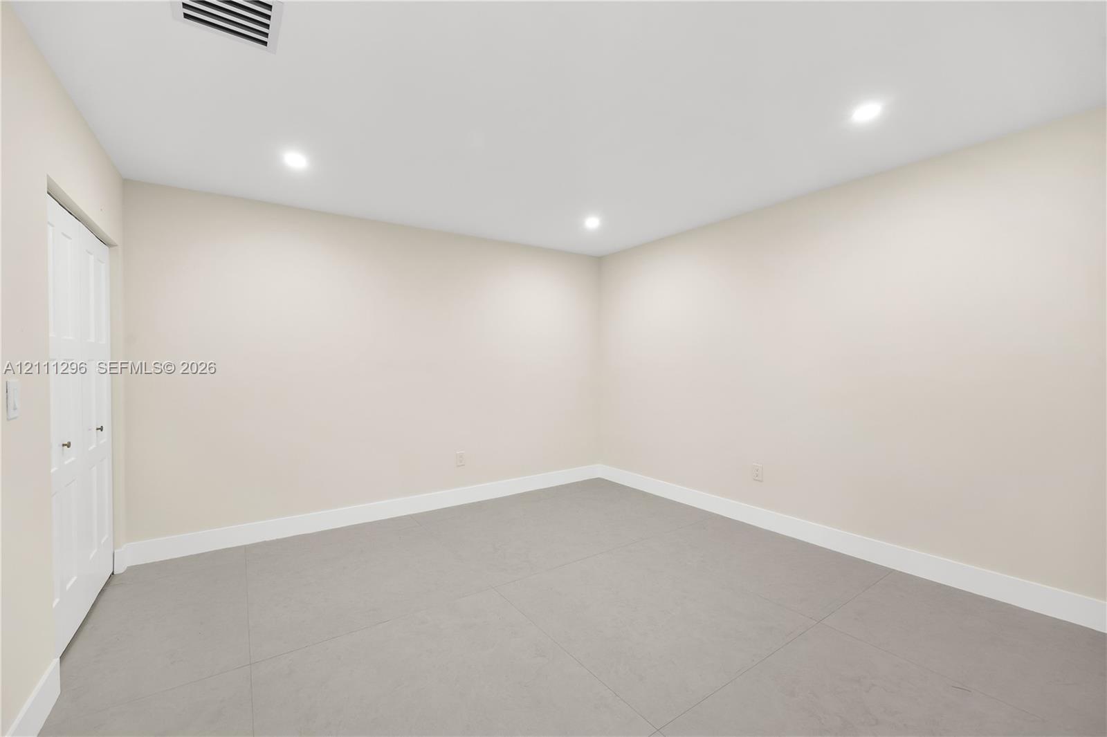 Neutral-toned room featuring large-format tile flooring, recessed ceiling lighting, and a dual-panel closet door