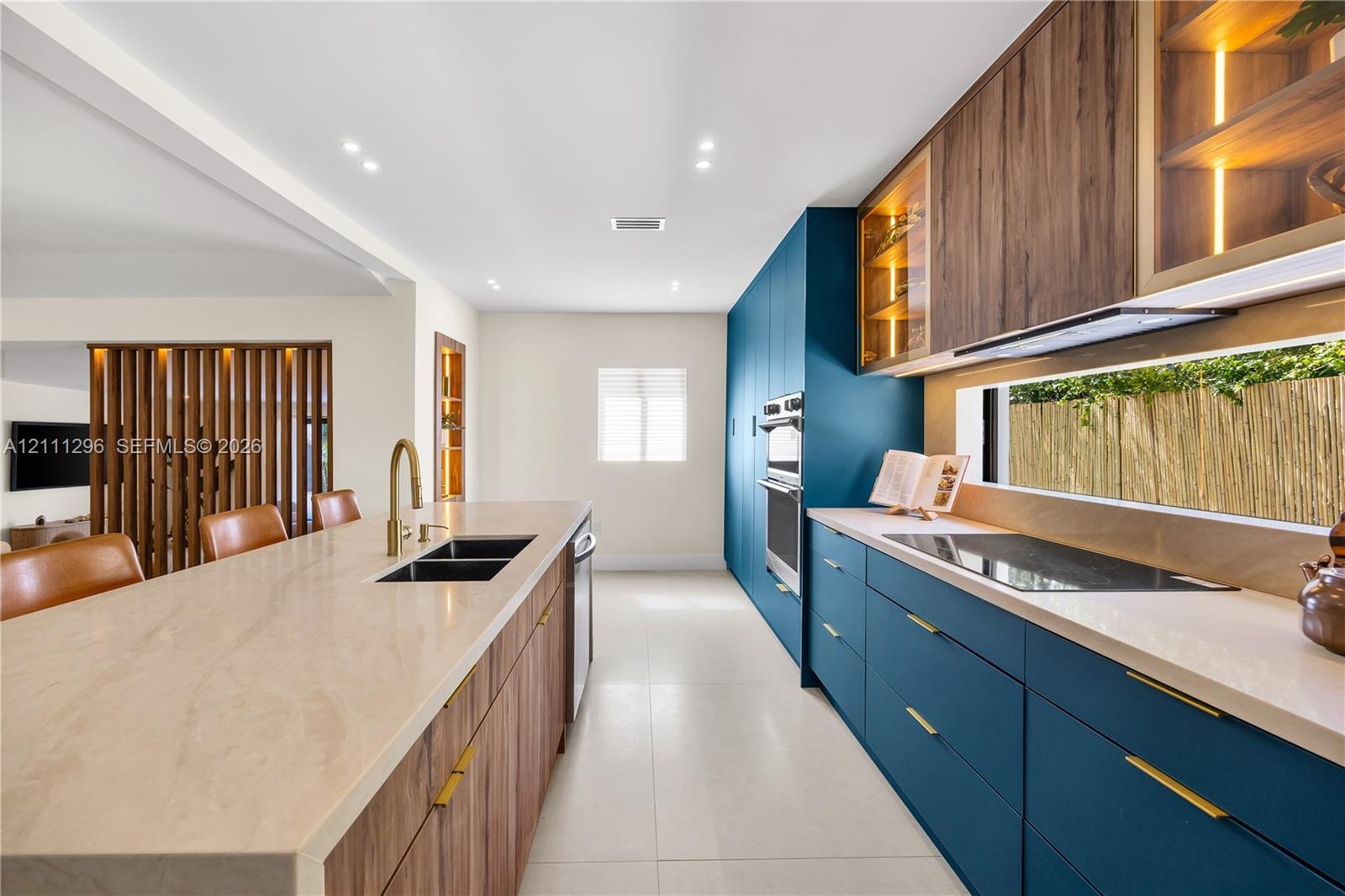 Modern kitchen featuring custom blue cabinetry, wood-finish lower cabinetry, stone-surface countertops, integrated under-cabinet lighting, and built-i