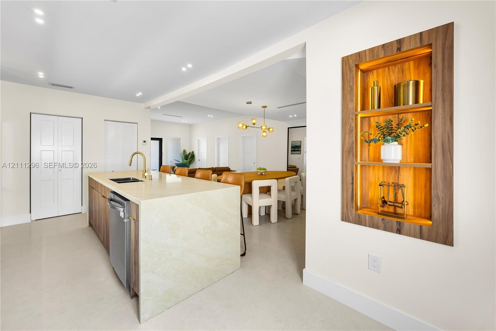 Kitchen island featuring a waterfall stone countertop, integrated stainless steel dishwasher, and a gooseneck faucet, accompanied by a recessed wall n