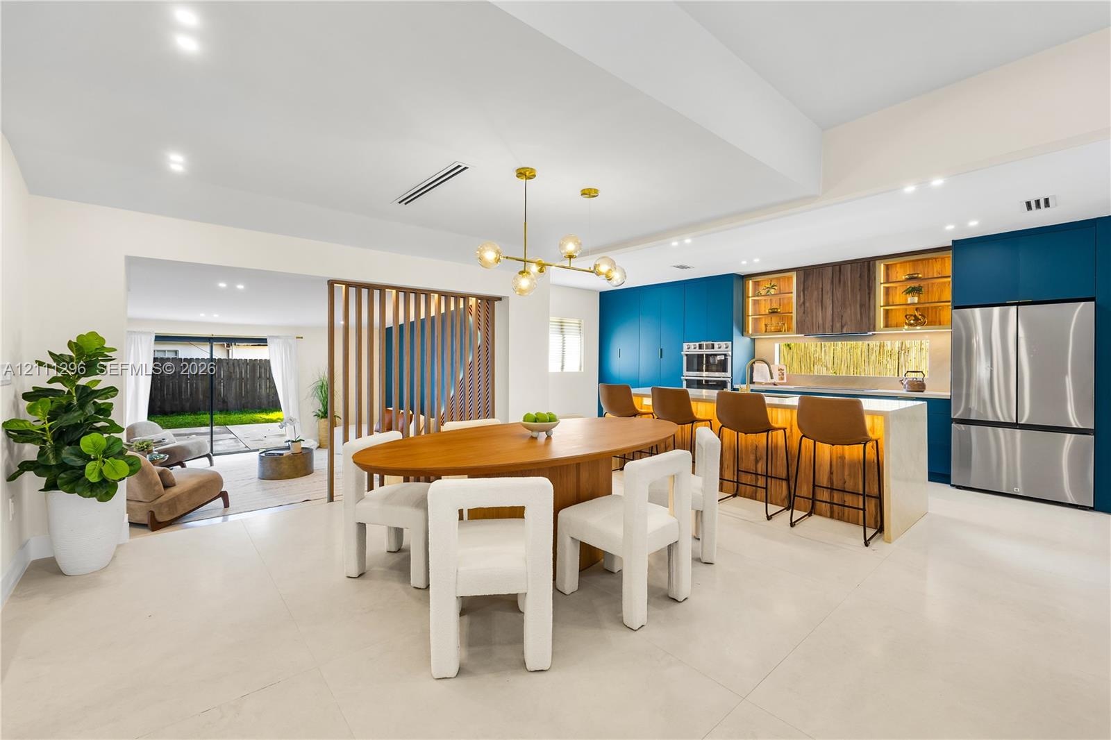 Open-concept kitchen and dining area featuring a central island with integrated stone countertop, modern blue cabinetry, wooden slat room divider, and