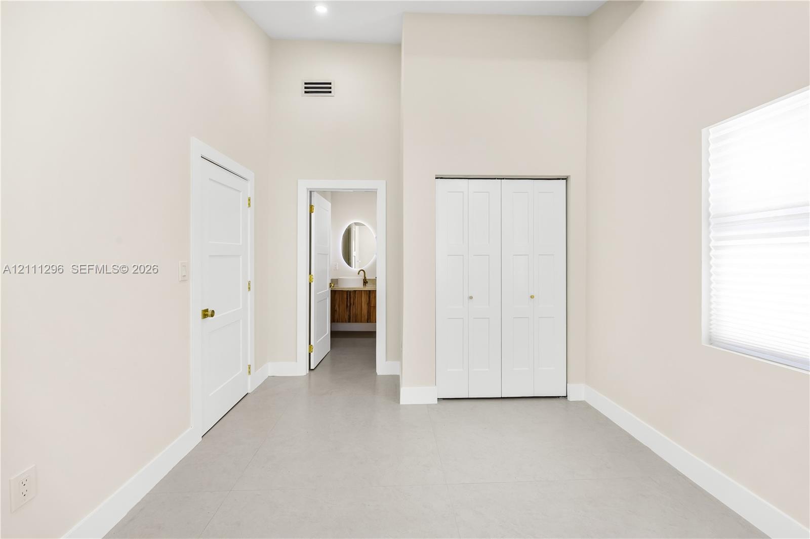 High-ceilinged room featuring neutral wall tones, large-format tile flooring, double-door closet cabinetry, and three-panel interior doors