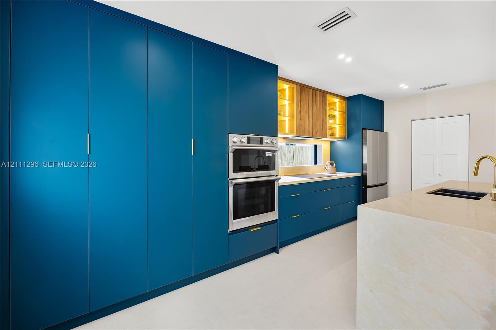 Kitchen featuring floor-to-ceiling blue cabinetry, built-in double wall ovens, wood-finish upper cabinets with integrated lighting, a stone-surfaced k