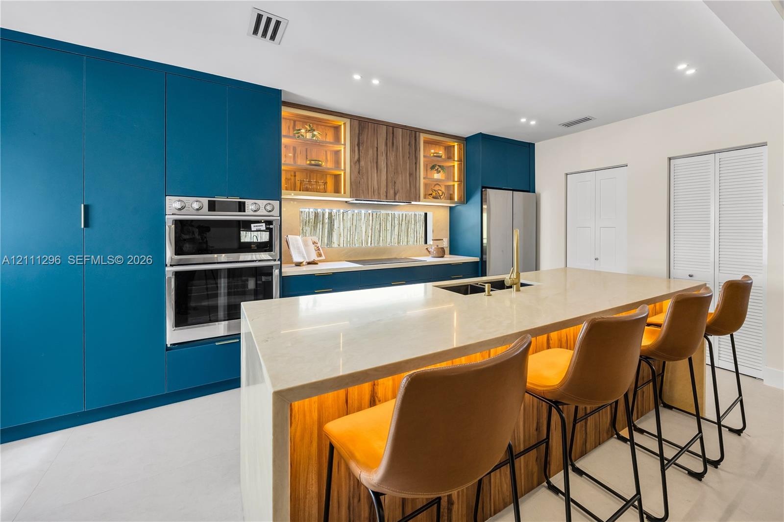 Kitchen featuring matte blue cabinetry, wood-finish upper cabinets with glass shelving, a large island with a stone-surface countertop, and built-in s