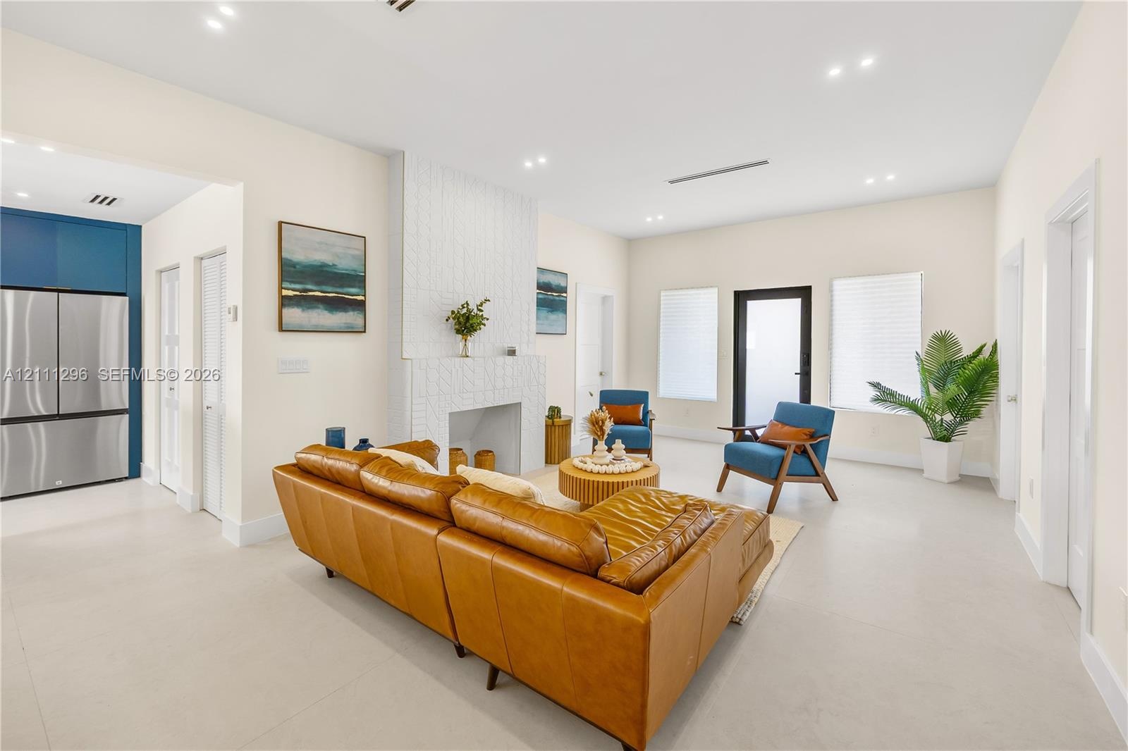 Living area featuring large-format tile flooring, recessed ceiling lighting, a textured floor-to-ceiling fireplace surround, and a glass-paneled exter