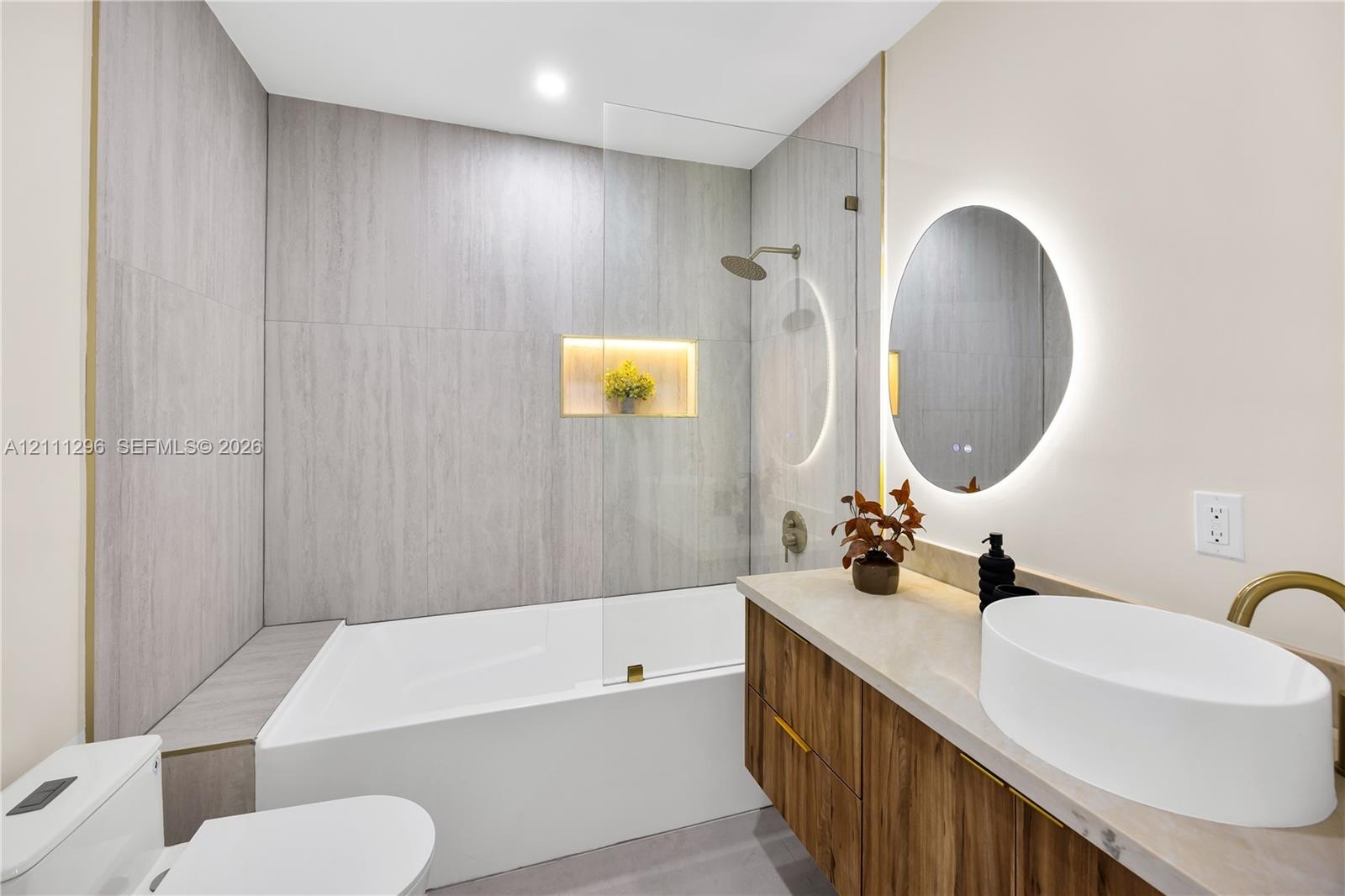 Bathroom featuring a wood-finish vanity with a vessel sink, quartz-style countertop, a walk-in shower with a glass panel and integrated recessed niche