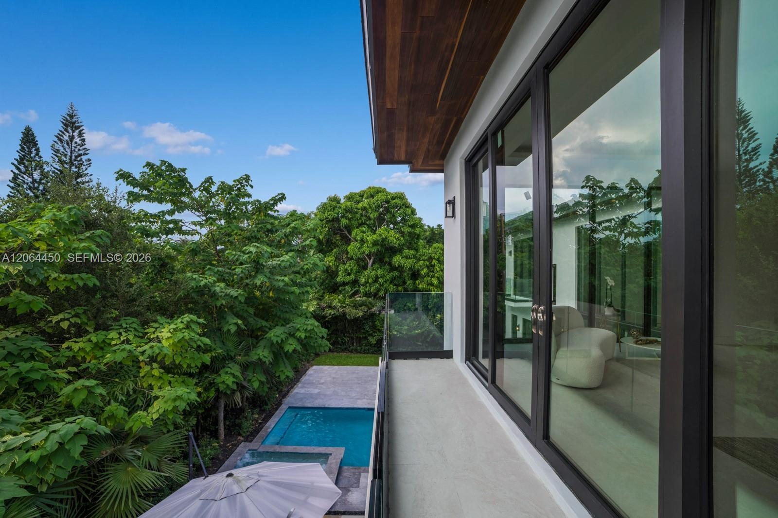 Balcony featuring a glass railing, wood-paneled ceiling, and floor-to-ceiling sliding glass doors, overlooking a private swimming pool with stone surr