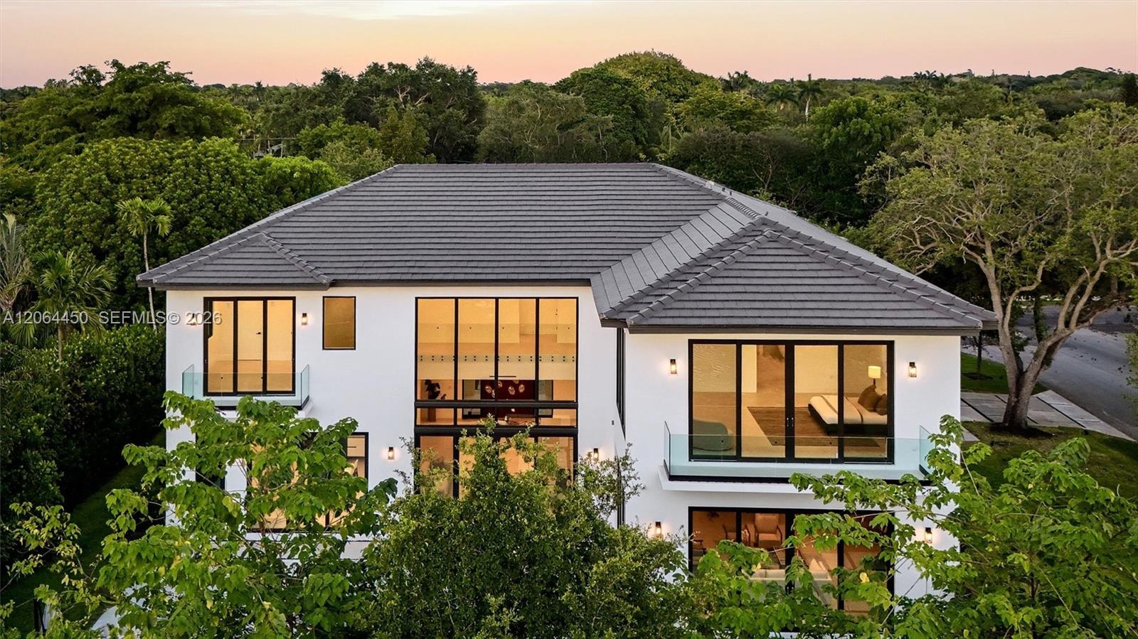 Two-story architectural residence featuring a tile roof, smooth white stucco exterior, expansive floor-to-ceiling windows with black metal framing, an