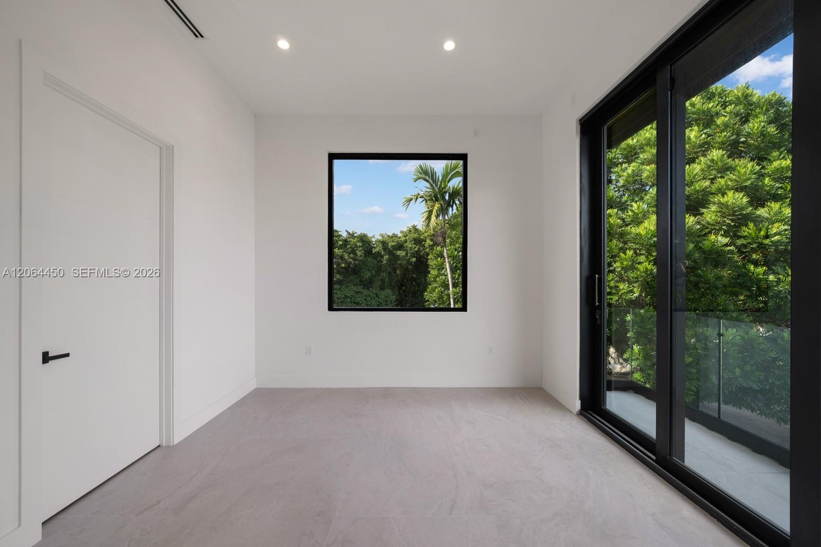 Interior room featuring neutral stone-finish flooring, recessed lighting, black-framed windows, and a sliding glass door providing access to a balcony