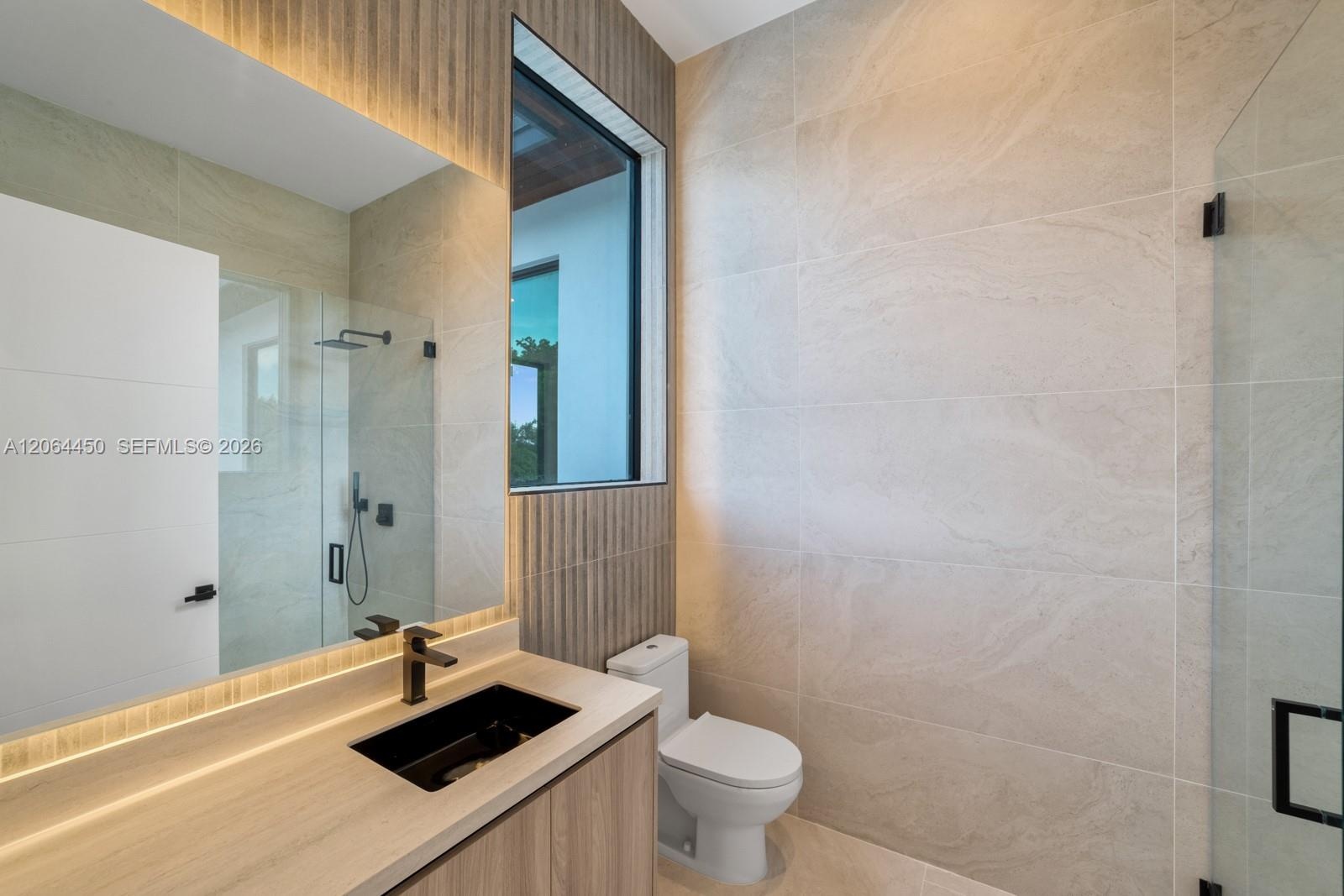 Bathroom featuring large-format stone-finish wall tiles, wood-finish vanity cabinetry, a rectangular vessel sink with matte black hardware, and an exp