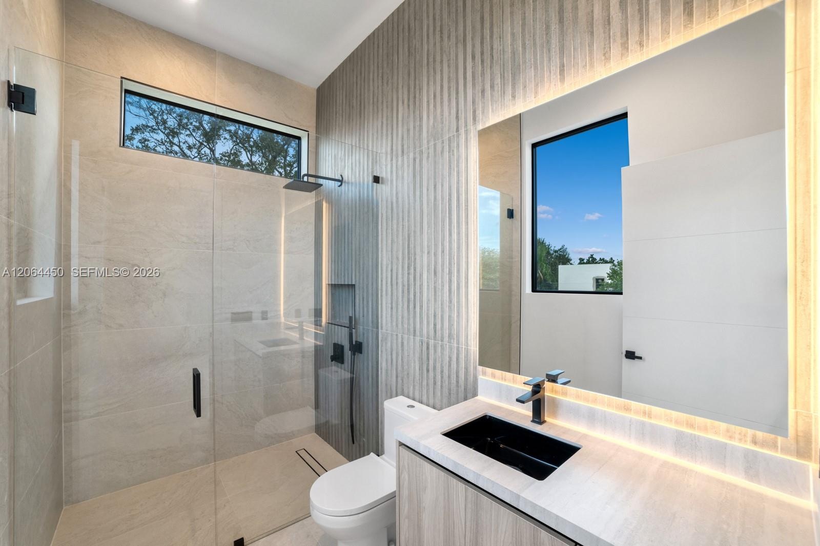 Walk-in shower with floor-to-ceiling tile, frameless glass enclosure, wall-mounted rain shower head, textured accent wall, and floating vanity with in