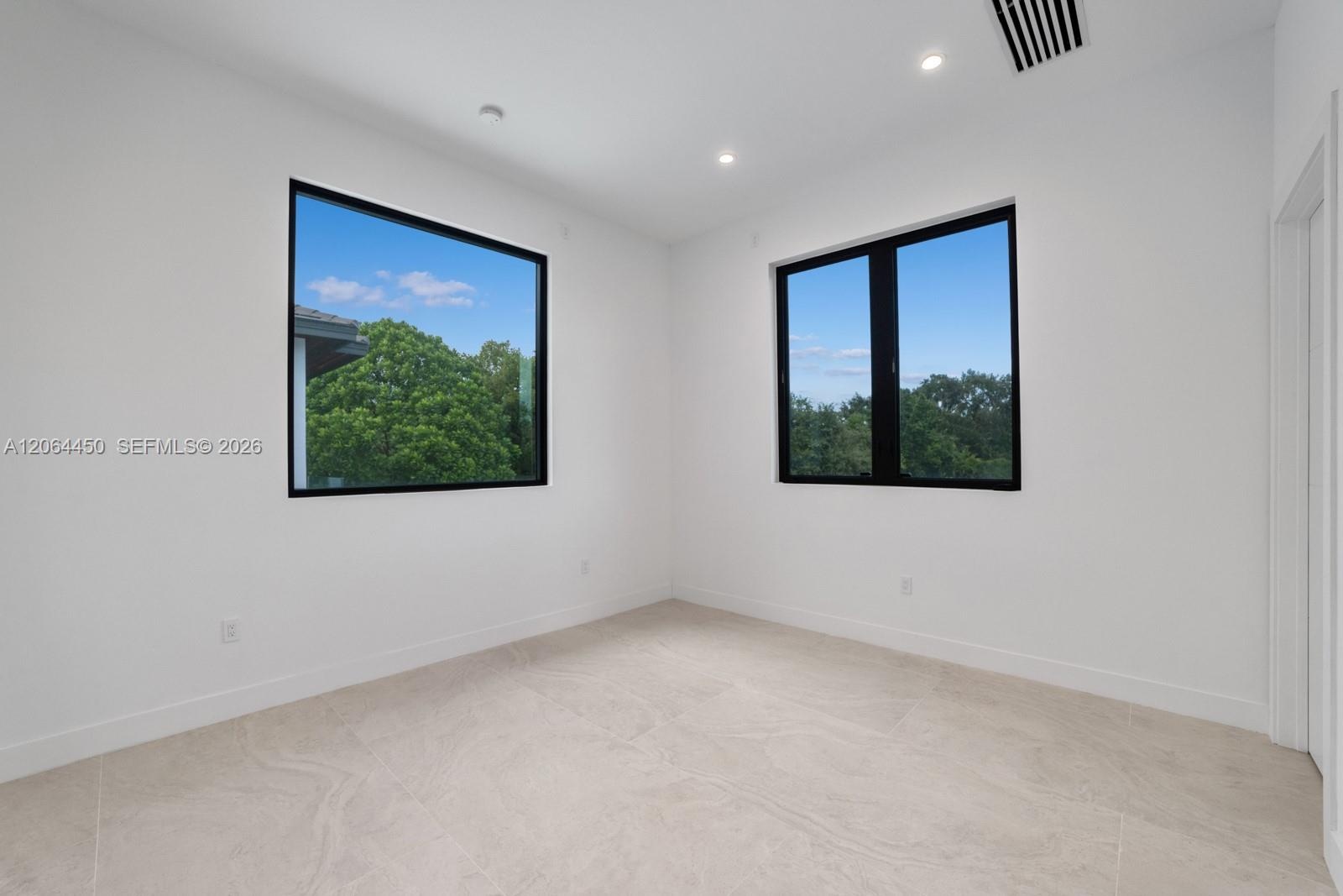 Interior room featuring high ceilings, large-format tile flooring, and dual windows with black frames