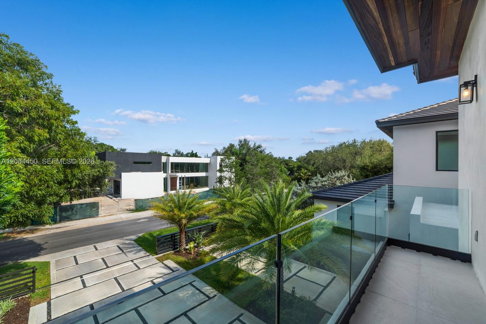 Second-story balcony with frameless glass railing, stone-finish flooring, wood-paneled ceiling, and wall-mounted exterior lighting