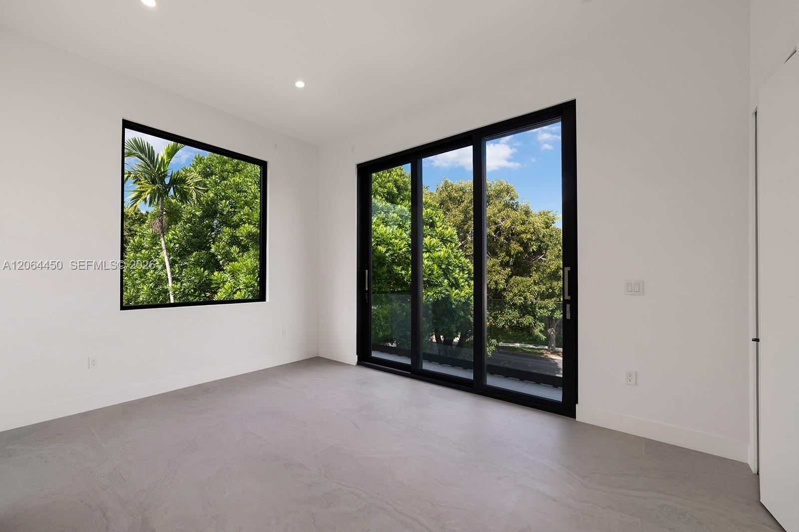 Interior space featuring large-format grey tile flooring, black-framed picture windows, black-framed sliding glass doors, and recessed ceiling lightin