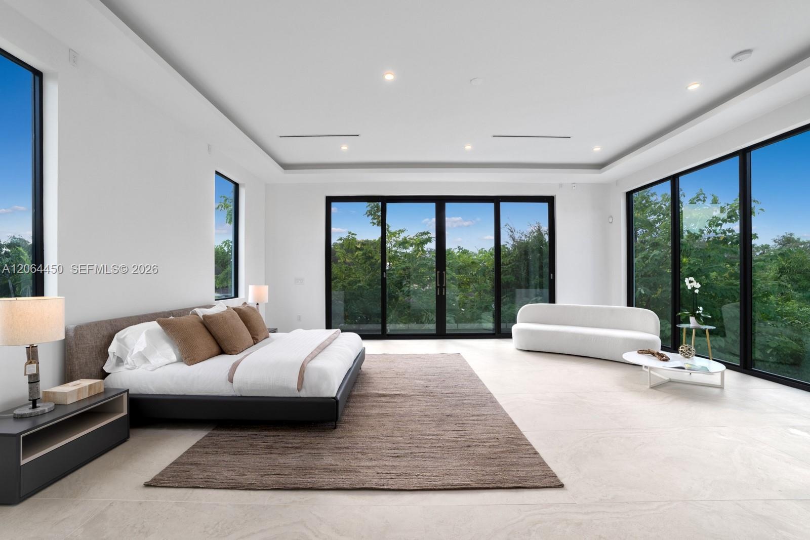 Open-concept room featuring floor-to-ceiling glass panel walls with black frames, recessed tray ceiling, neutral stone-finish flooring, and integrated