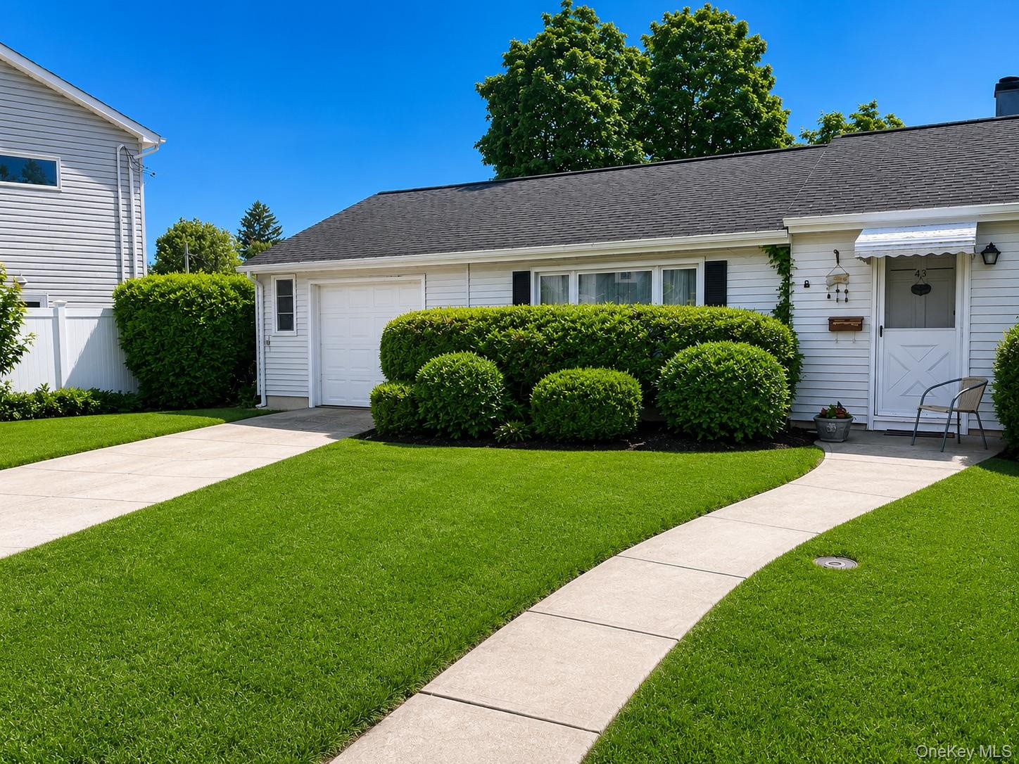 White siding exterior with a dark shingle roof, complemented by a concrete driveway and walkway