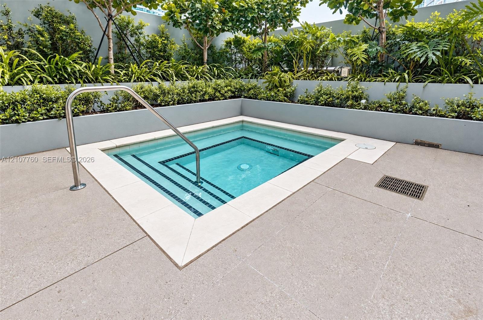 In-ground pool with integrated stepped entry and stainless steel handrail, bordered by stone-finish coping and tiered landscape planters with mature s